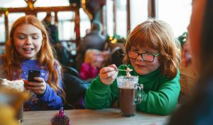 Two children sitting in the Alpine Lodge, one is having a freshly made Hot Chocolate
