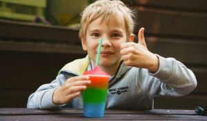 A child holding a mult-coloured slushy, they are giving it a thumbs up.