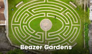 An overhead view of a maze made of paving stones with grass planted around them. There is a large paved circle in the centre of the maze