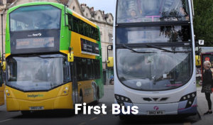 Two buses are travelling down a road. One has pulled over to pick up a passenger. The bus on the left is orange and green and the bus on the right is purple, pink and white. Both buses have the ‘First Bus’ logo on them